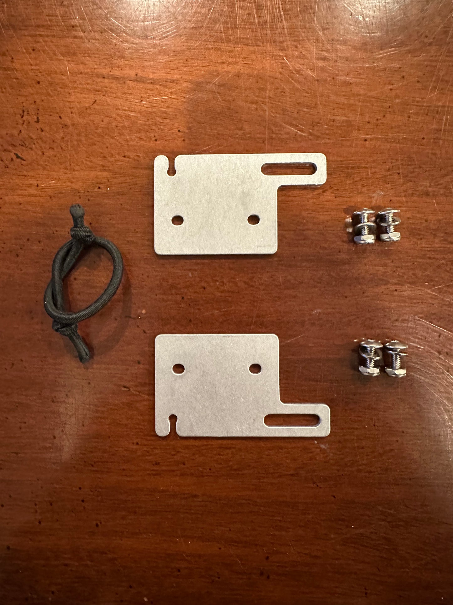 Two metal brackets and a black cord on a wooden surface